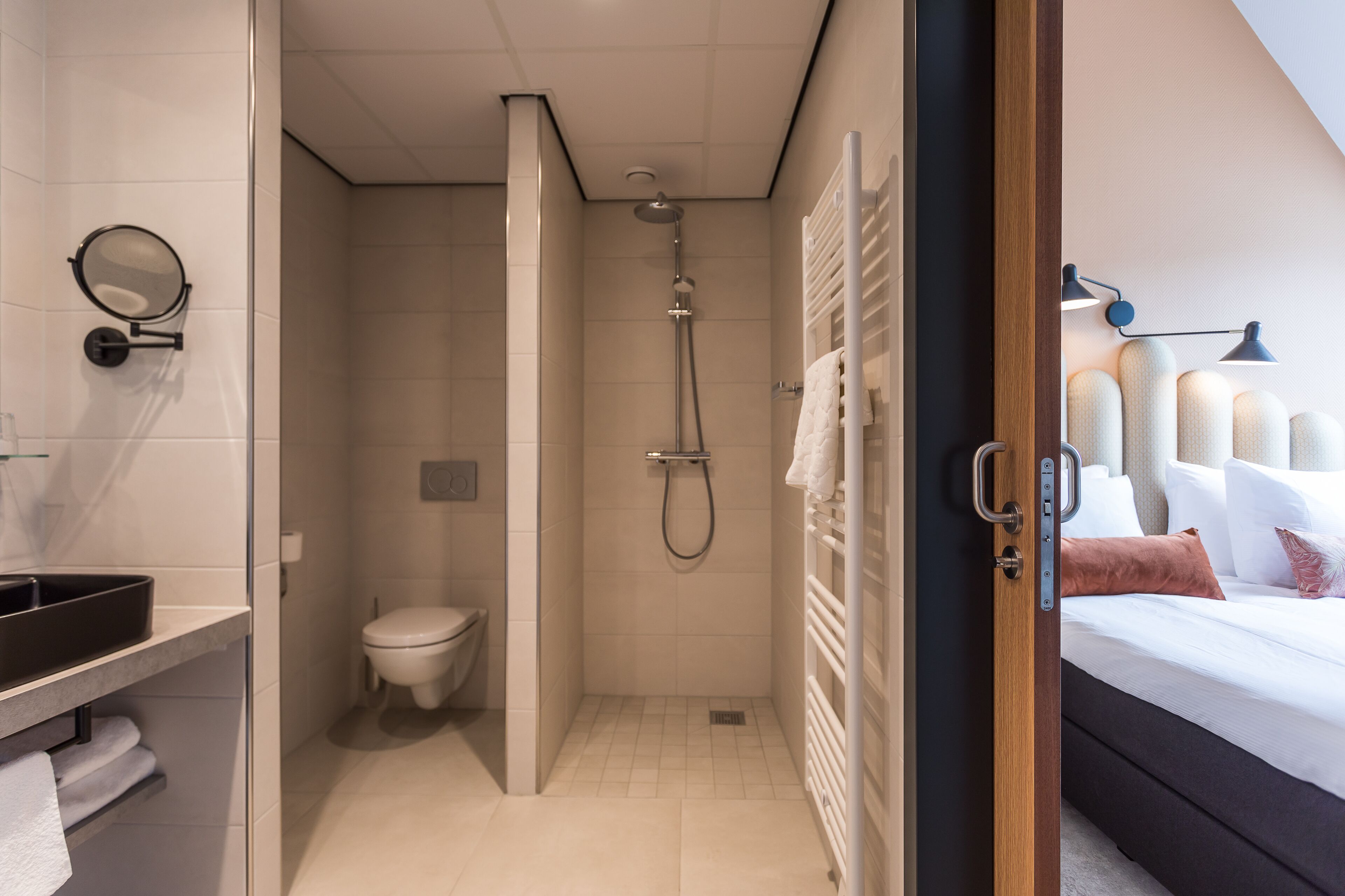 A modern bathroom with a shower, toilet, and a bed with a nightstand.
