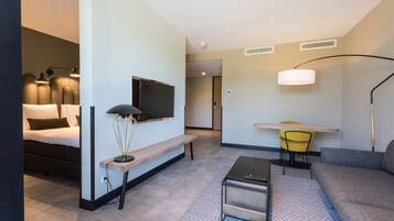 A modern hotel room with a bed, a desk, a sofa, a lamp, and a TV.