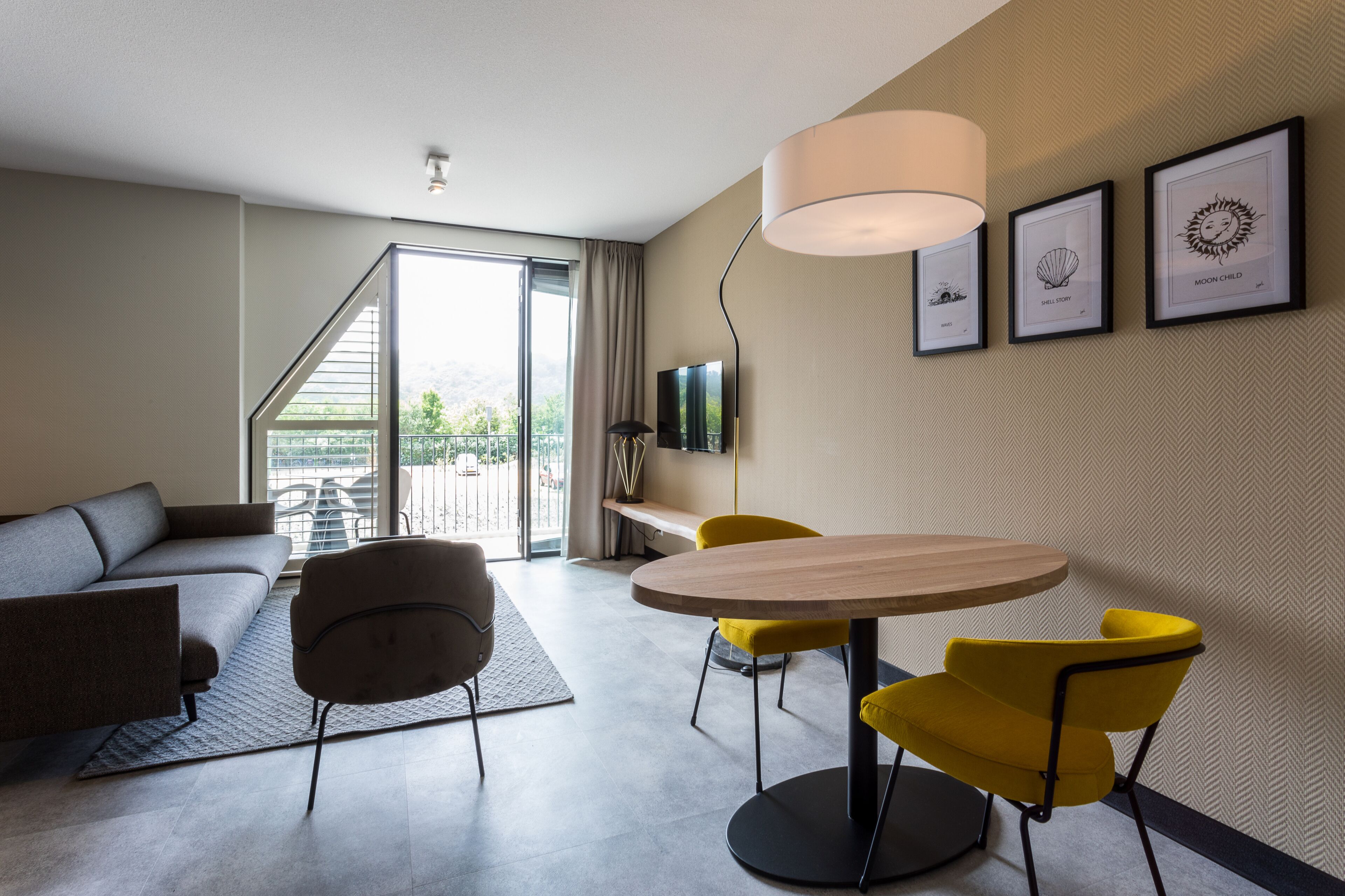 Una sala moderna con un sofá, una mesa de comedor con sillas amarillas, un televisor y obras de arte enmarcadas en la pared.