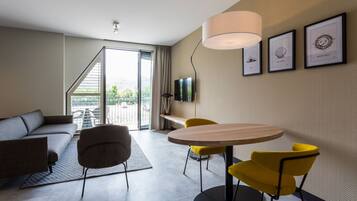 Una sala moderna con un sofá, una mesa de comedor con sillas amarillas, un televisor y obras de arte enmarcadas en la pared.