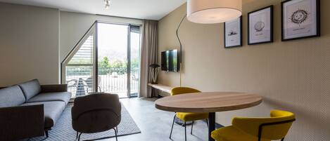 Una sala moderna con un sofá, una mesa de comedor con sillas amarillas, un televisor y obras de arte enmarcadas en la pared.