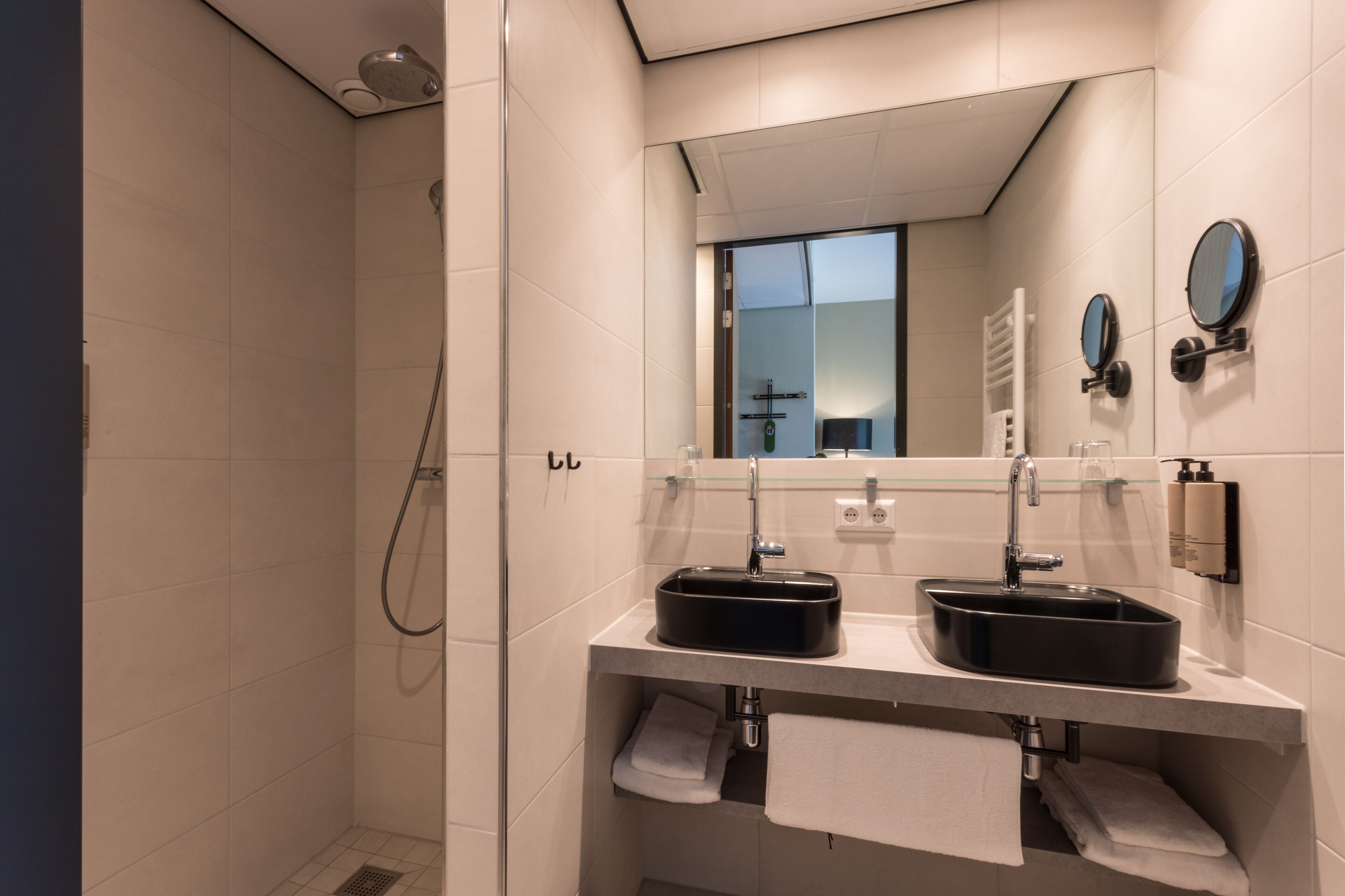 Ein modernes Badezimmer mit zwei Waschbecken, einer Duschkabine aus Glas und einem großen Spiegel.