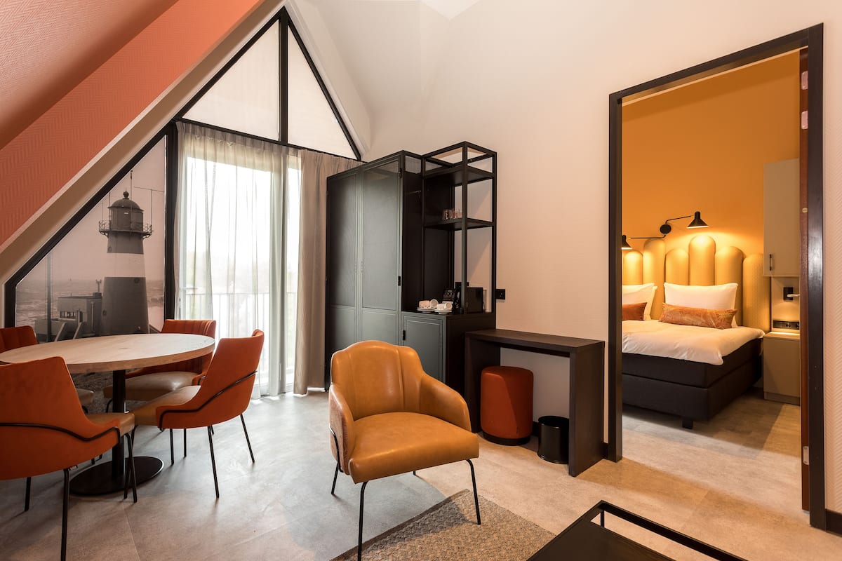 Una camera d'albergo moderna con zona pranzo, divano, letto e scrivania.