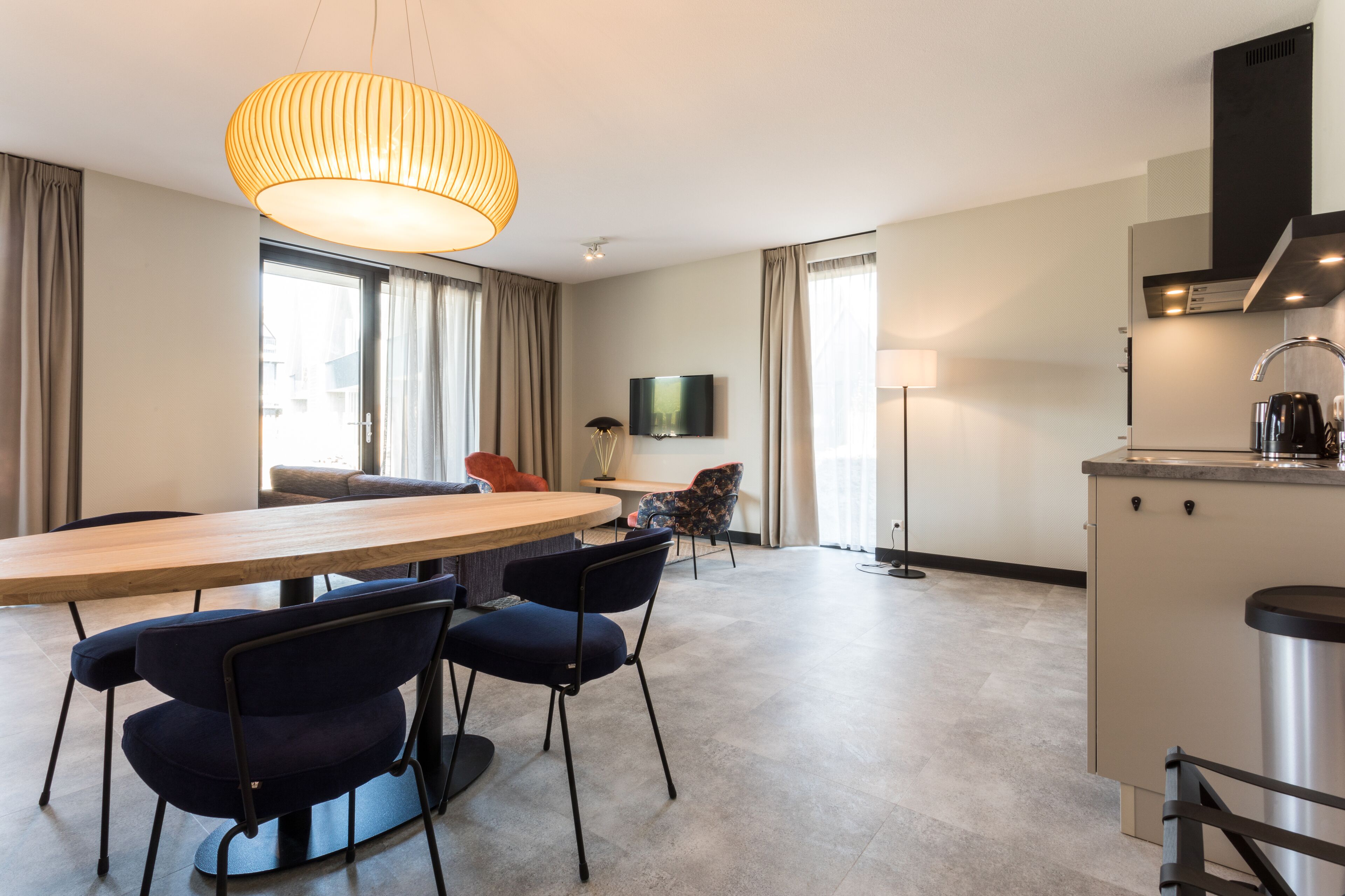A modern hotel room with a dining area, a kitchen, and a large window.