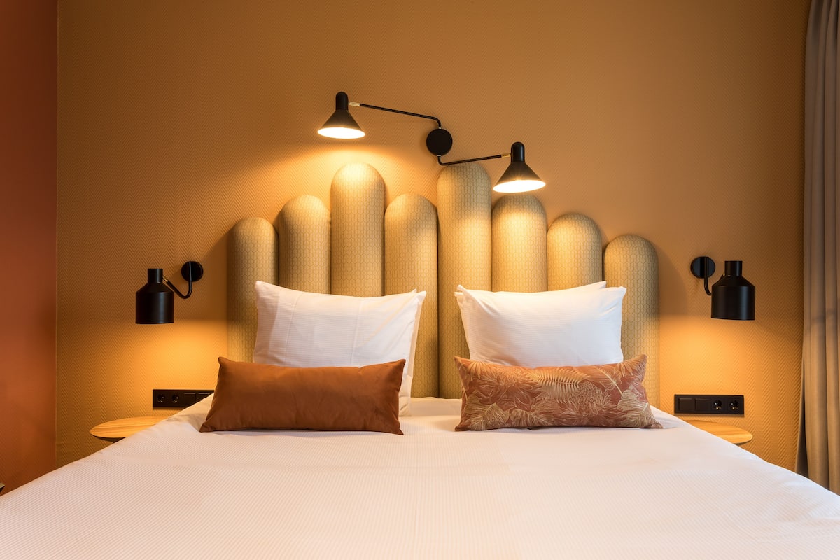Camera d'albergo con un letto grande, due lampade ai lati e una parete testurizzata dietro il letto.