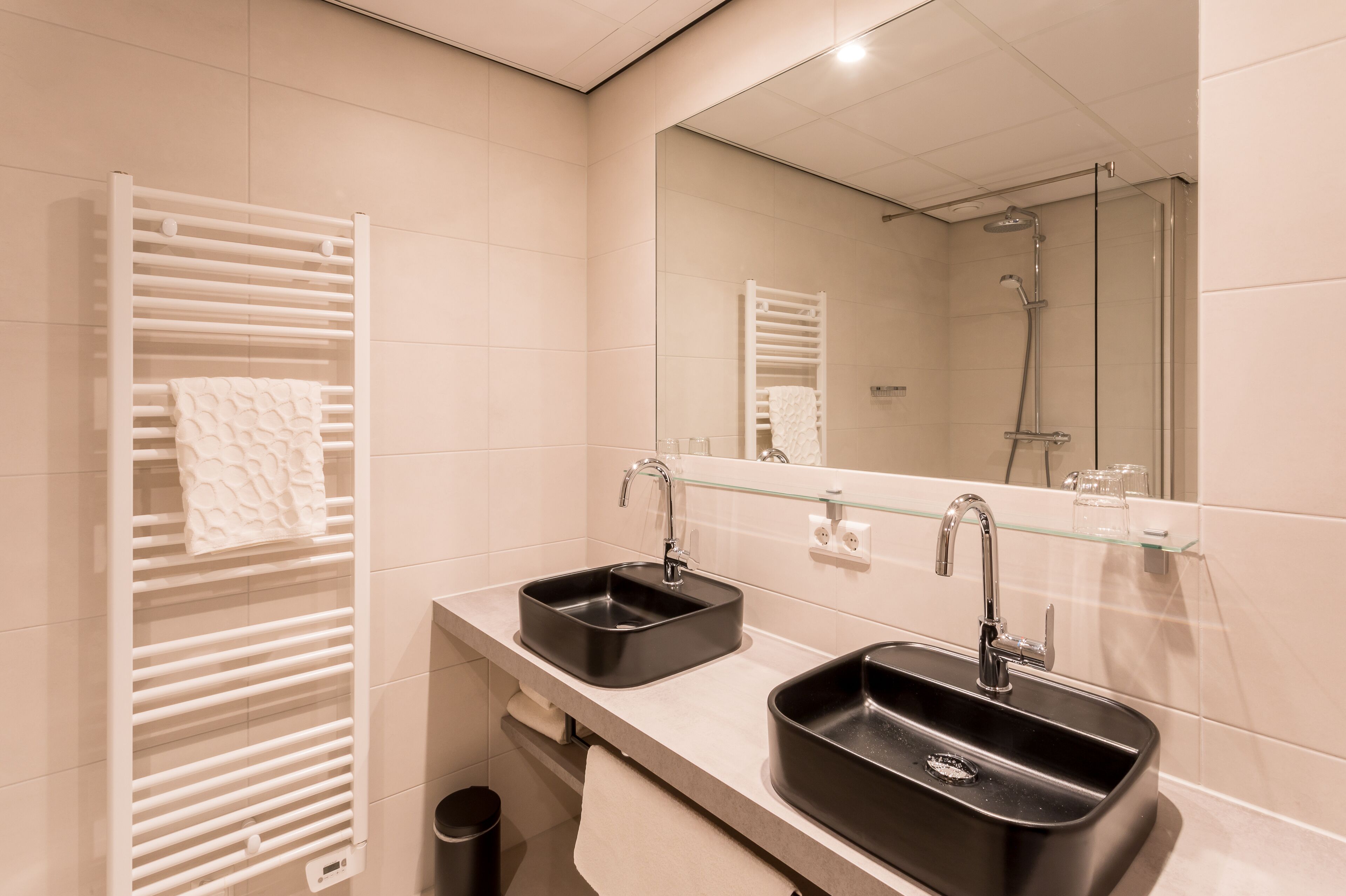 A modern bathroom with two sinks, a glass shelf, and a large mirror.