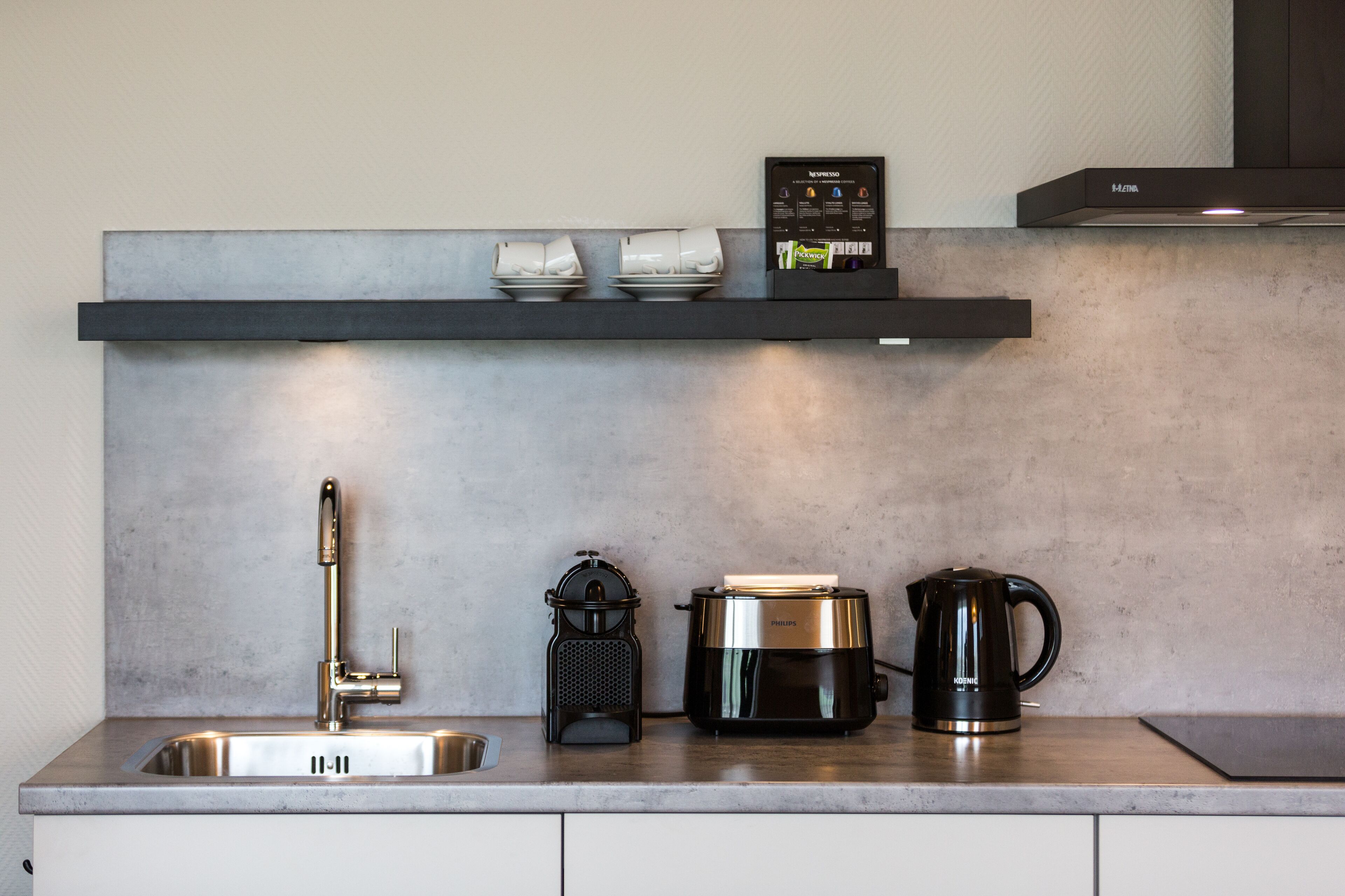 Une cuisine moderne dotée d’un évier en acier inoxydable, d’une machine à café, d’une bouilloire et d’une machine à expresso intégrée, le tout installé sur un plan de travail.