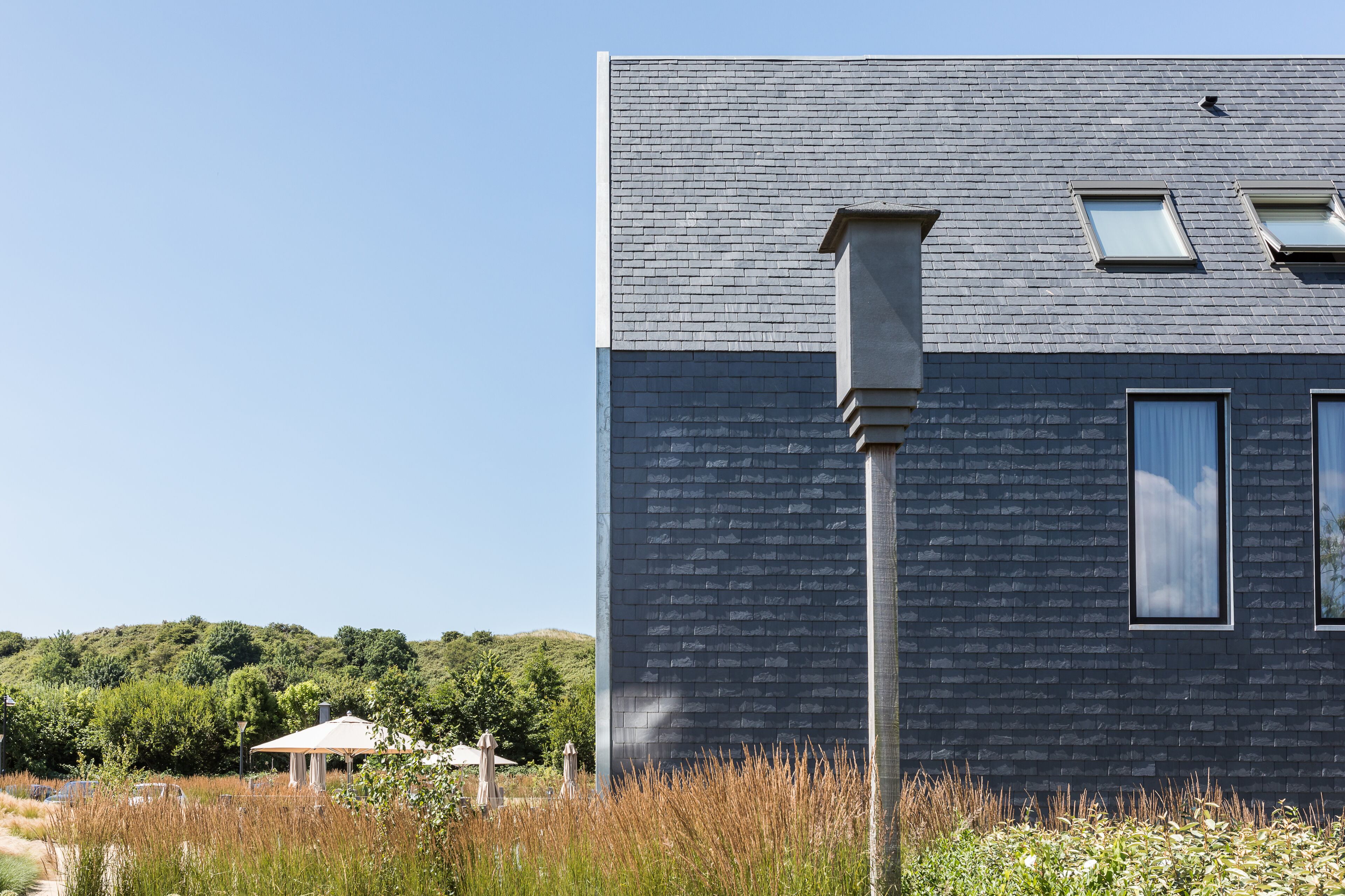 A modern building with a dark brick facade, two windows, and a chimney.