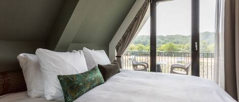 A hotel room with a large bed, a view of the outdoors through a sliding glass door, and a balcony with chairs.