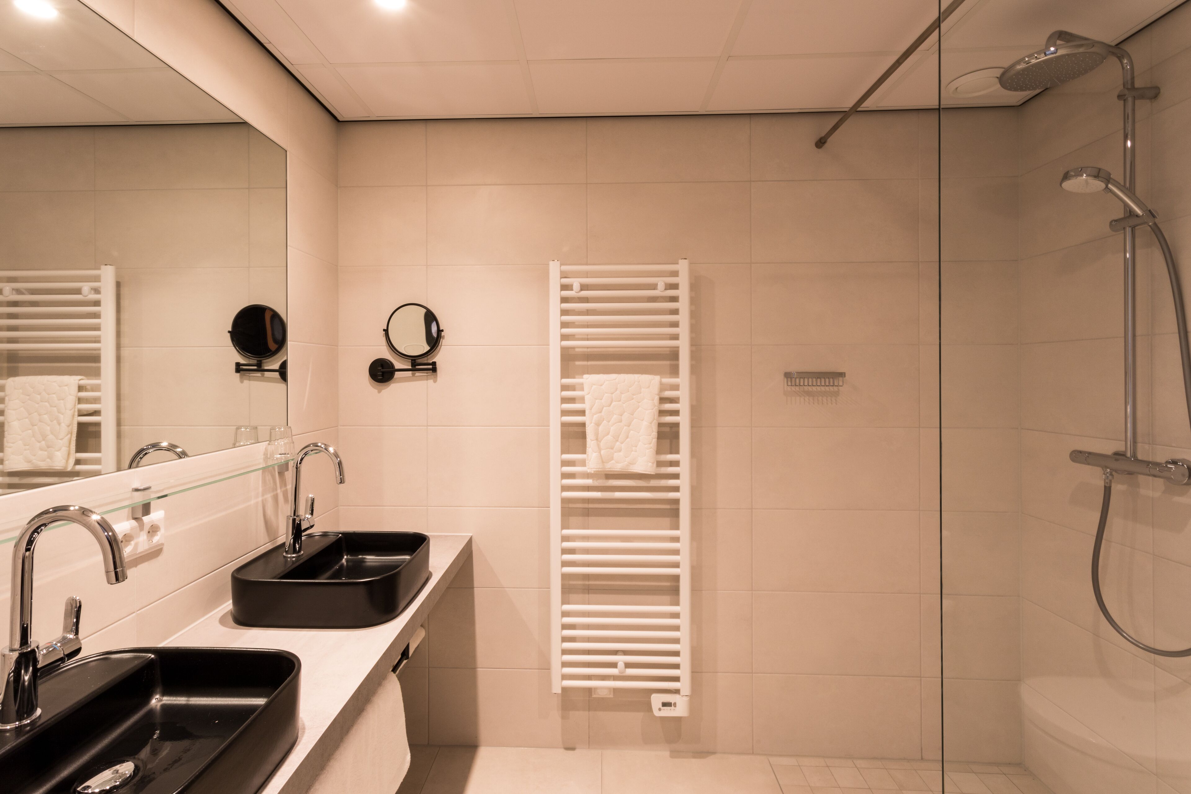 Une salle de bain moderne avec deux vasques, une douche à parois de verre et un porte-serviettes.