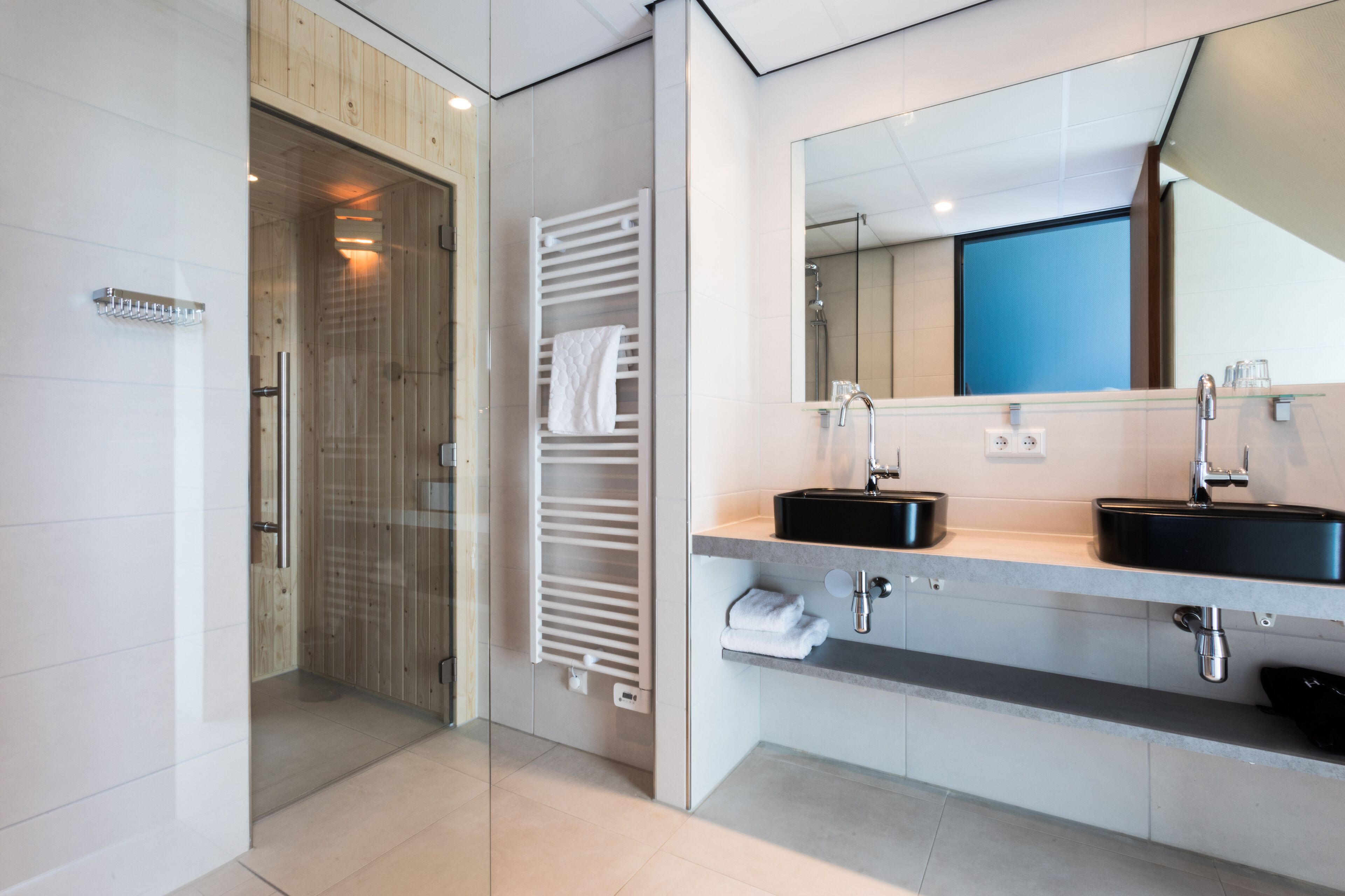 A modern bathroom with two sinks, a large mirror, and a glass shower enclosure.