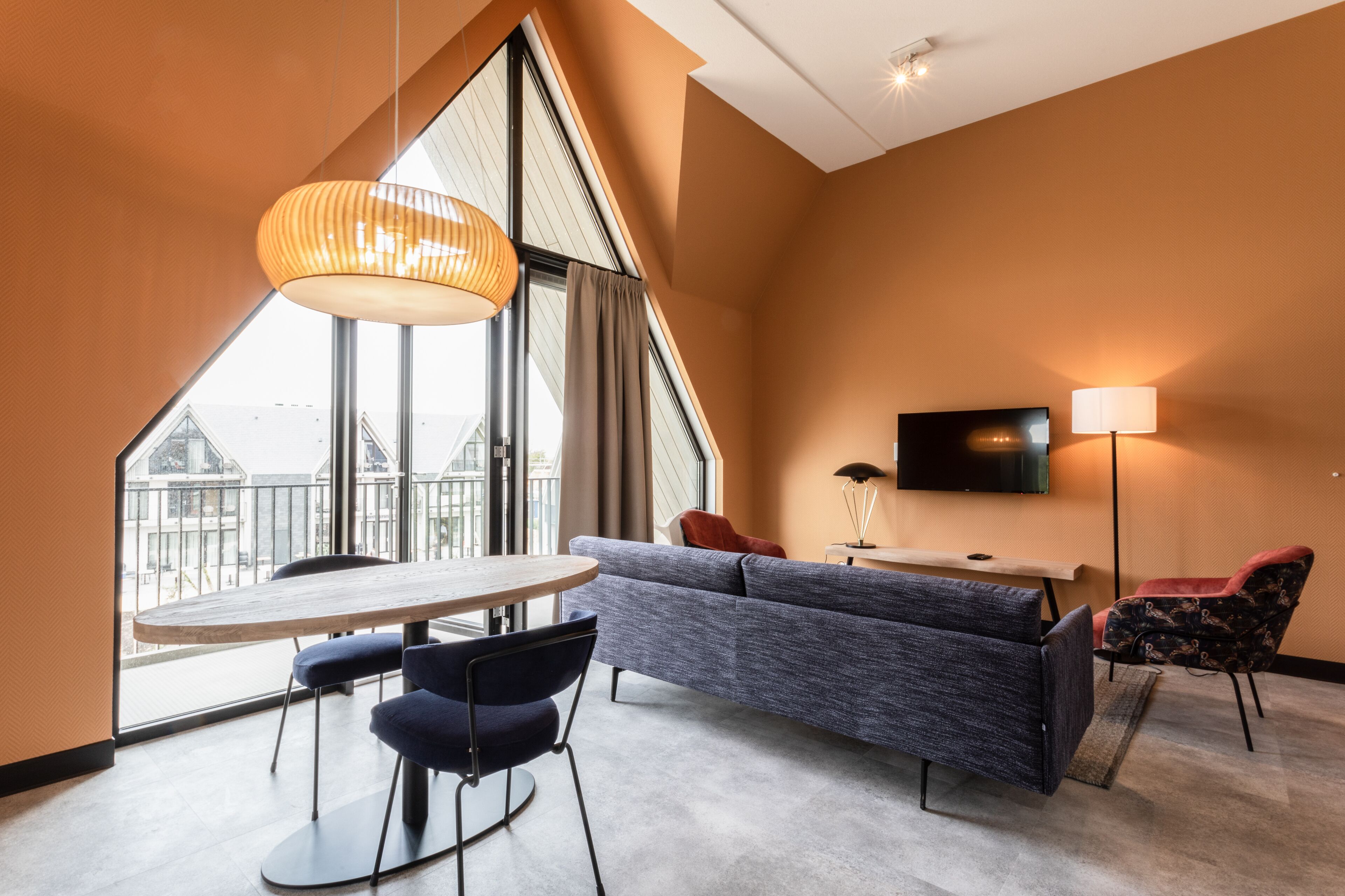 Een moderne hotelkamer met een groot raam, een bank, een televisie en een eethoek.