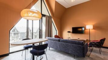 Een moderne hotelkamer met een groot raam, een bank, een televisie en een eethoek.