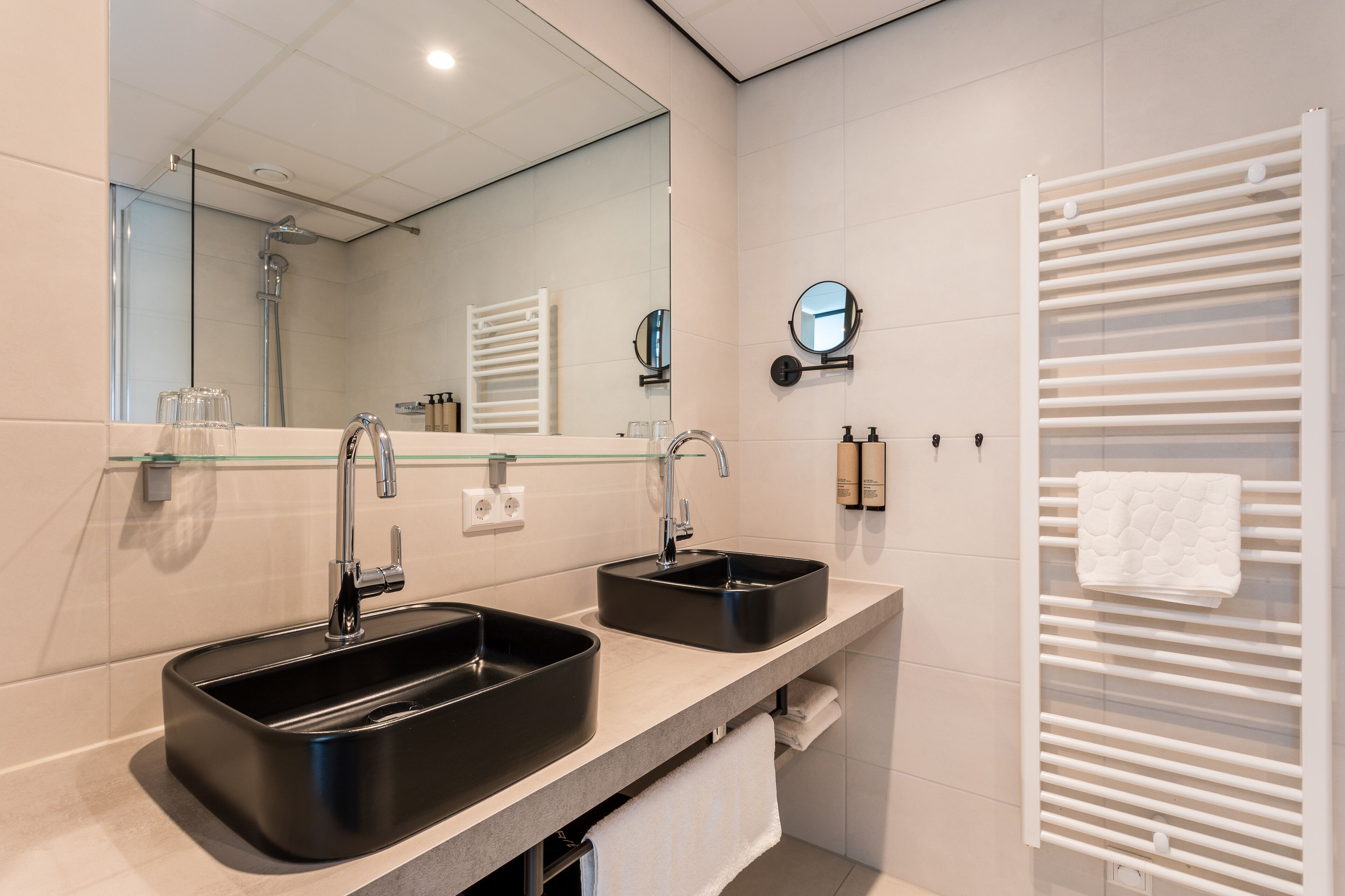 A modern bathroom with two black sinks, a glass shelf, a towel rack, and a mirror.