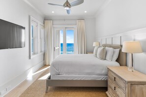 Una habitación de hotel moderna con una cama grande, un televisor de pantalla plana, un ventilador de techo y vistas al océano.
