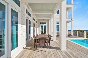 A covered outdoor dining area with a wooden table and chairs, large windows, and a view of the ocean. - 30A Stunner! Gulf Views, Private Pool, Beach & Golf Cart | Fall Now Booking! (Santa Rosa Beach)