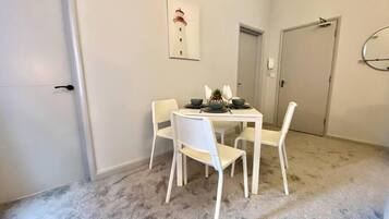 Un comedor con una mesa blanca y cuatro sillas, un cuadro en la pared, y piso alfombrado.