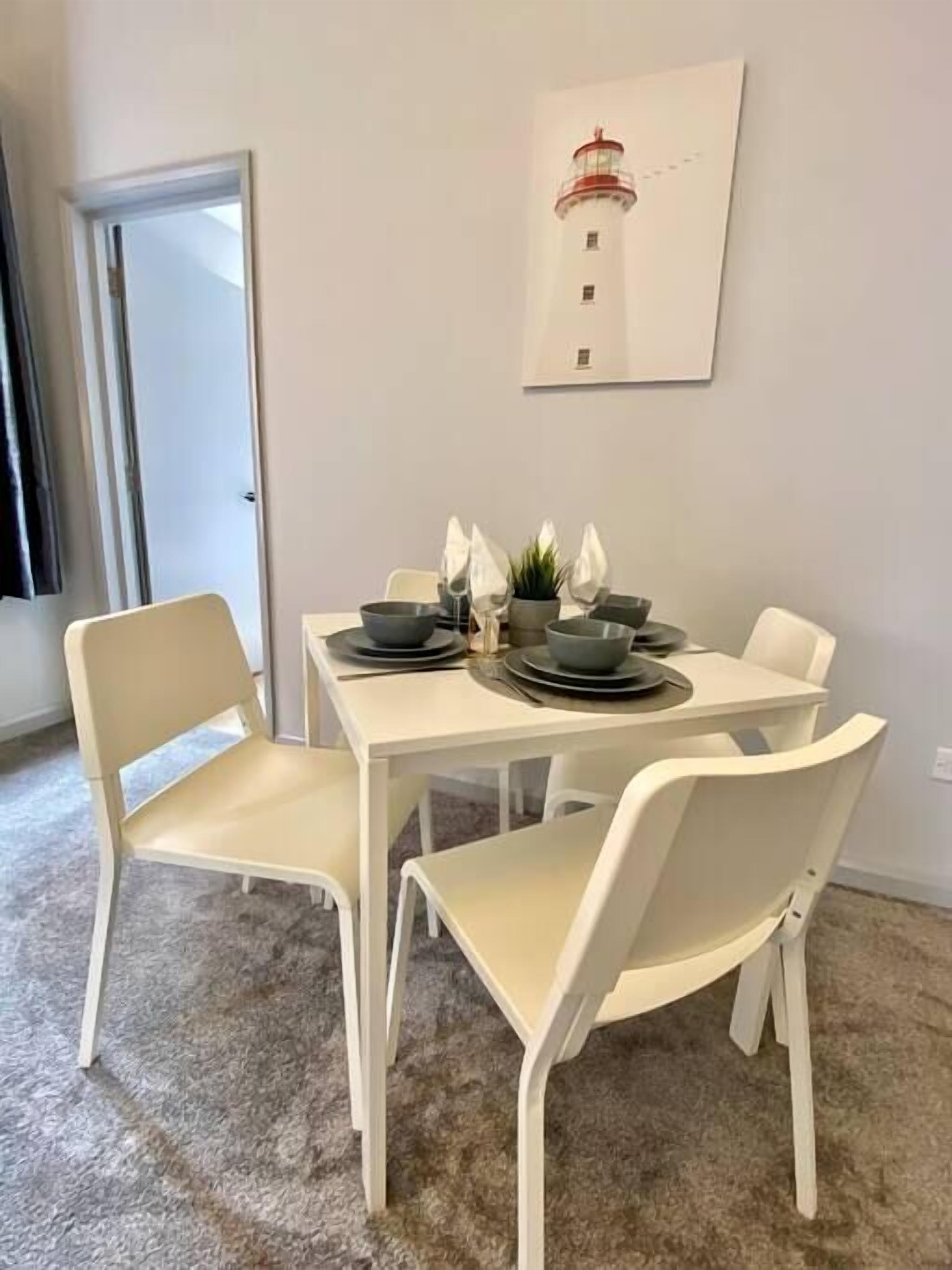 A dining area with a white table and four chairs, a framed picture on the wall, and a door leading to another room.
