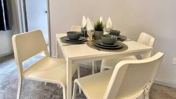 A dining area with a white table and four chairs, a framed picture on the wall, and a door leading to another room.