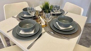 Neljälle katettu pöytä, jossa on harmaat lautaset, kulhot ja viinilasit. Pöydällä on myös pieni kasvi ja ananaksesta tehty koristeellinen asetelma.