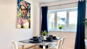 A dining area with a table set for four, white chairs, a blue tablecloth, and a painting on the wall.