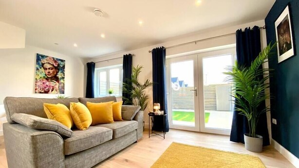 A modern living room with a grey sofa, yellow cushions, a yellow rug, and a large window with curtains.