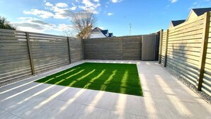 A backyard with a green artificial turf, surrounded by wooden fences and a clear sky.