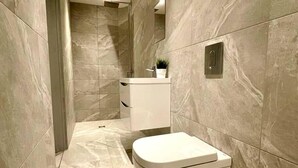 Ein modernes Badezimmer mit Toilette, Waschbecken und Duschbereich, mit Marmorwänden und -boden.
