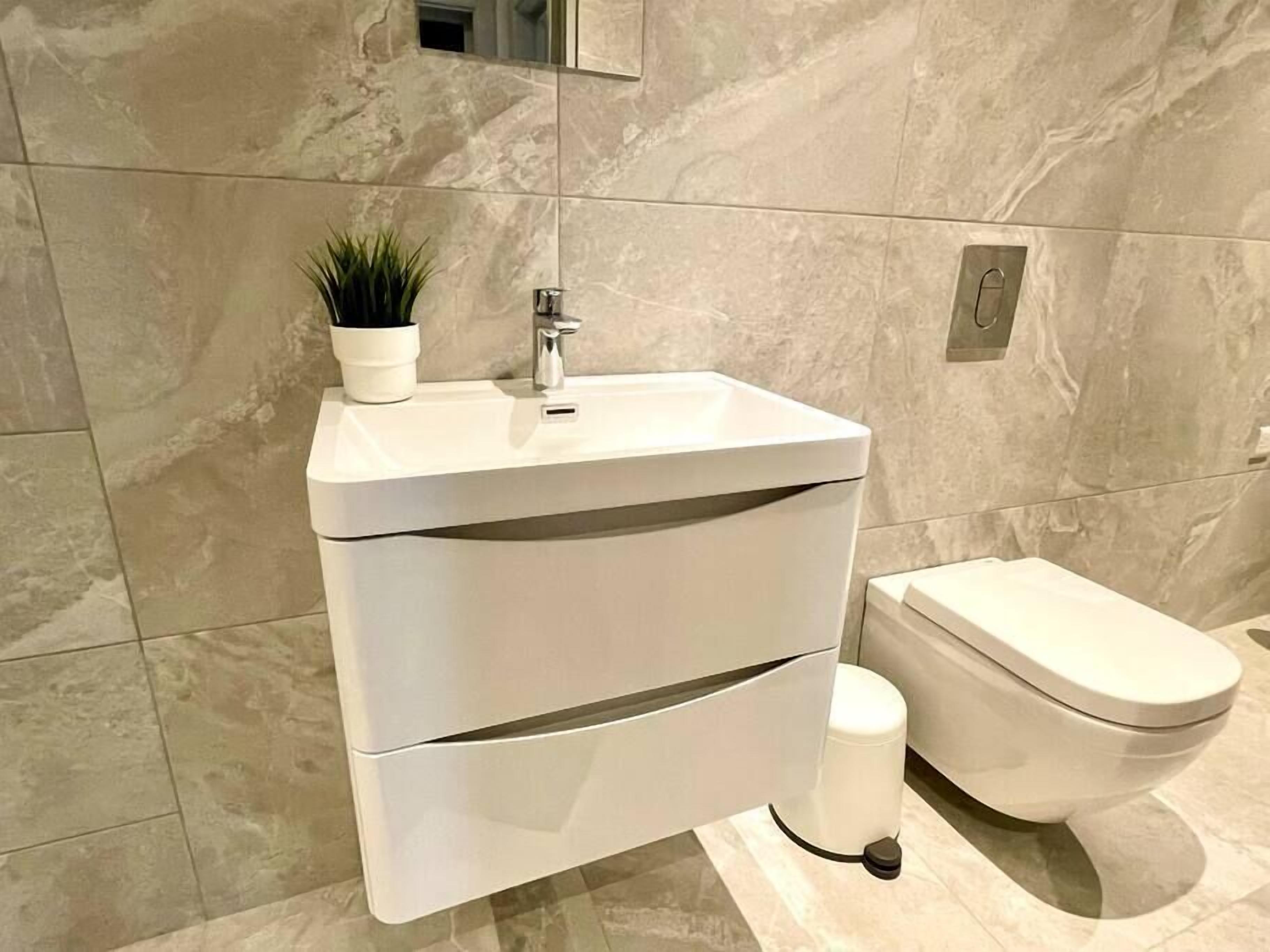 A modern bathroom with a white sink, a toilet, and a marble wall.