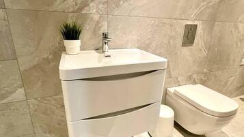 A modern bathroom with a white sink, a toilet, and a marble wall.