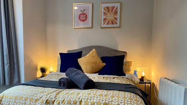 A neatly made bed with a patterned bedspread, two pillows, and a rolled towel. There are two framed pictures on the wall above the bed. - Funky Apartment - 5 minute walk to the beach! (Westbourne)