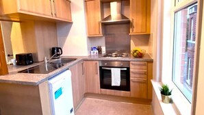 A compact kitchen with wooden cabinets, a stainless steel range hood, a built-in oven, and a small window with a plant. - Funky Apartment - 5 minute walk to the beach! (Westbourne)