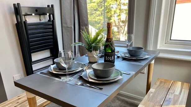 A dining table set with plates, bowls, cutlery, and a bottle of champagne. - Trendy Apartment - 5 minute walk to the beach! (Bournemouth)