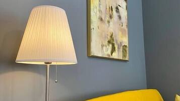 Une pièce avec un canapé jaune, un lampadaire et un tableau accroché au mur.