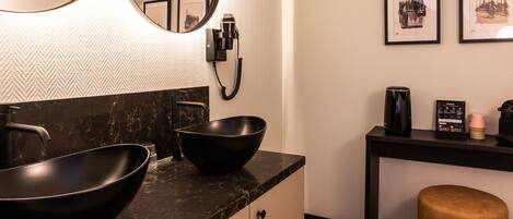 A modern bathroom with a black sink, a mirror, a hairdryer, and framed pictures on the wall.