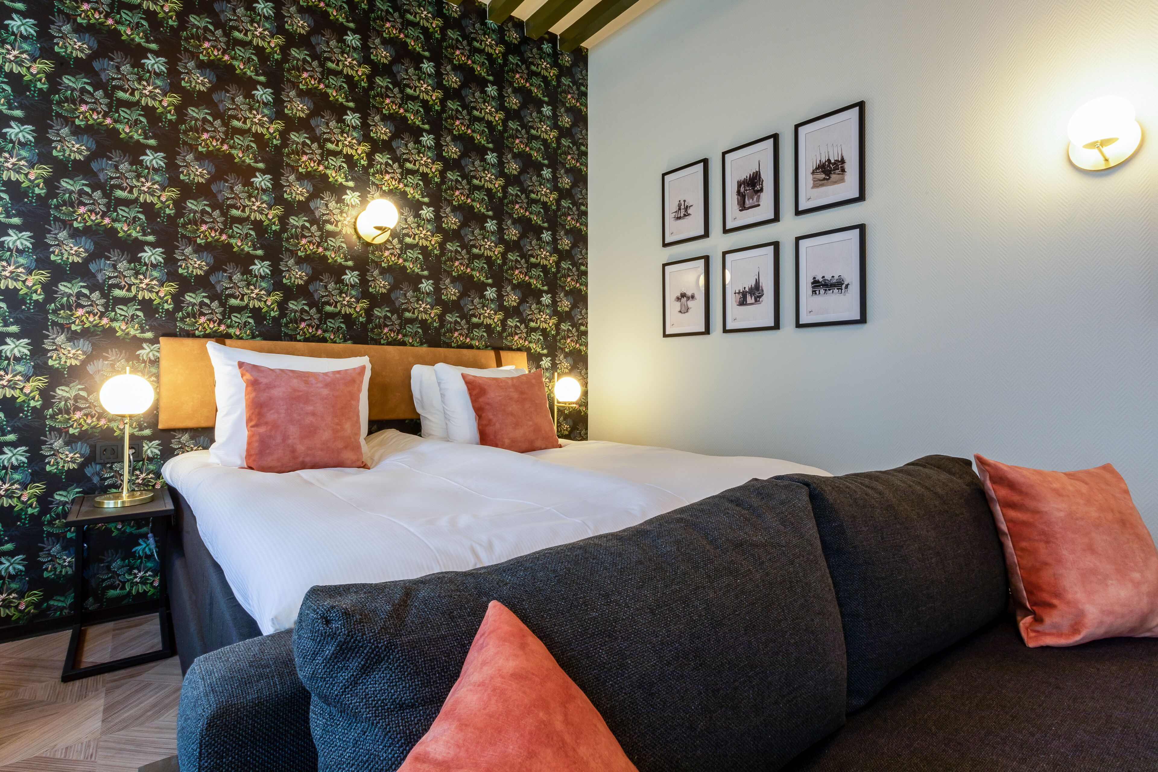 Une chambre d’hôtel avec un lit, une table de chevet, un mur orné de tableaux et un papier peint à motifs.