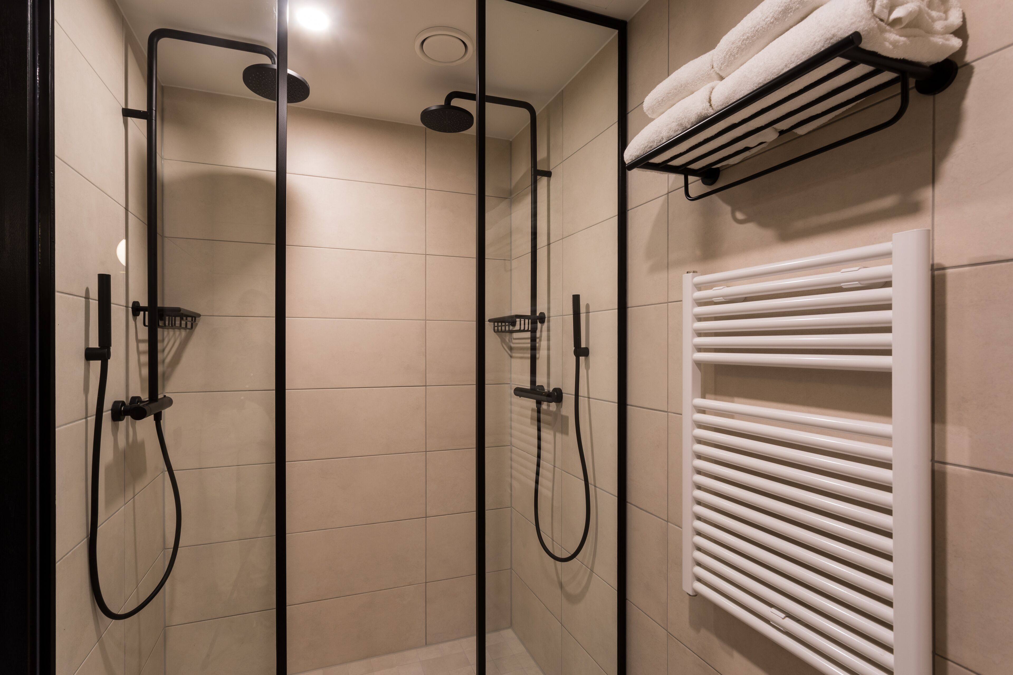 A modern bathroom with a glass-enclosed shower, a white towel rack, and a built-in towel warmer.