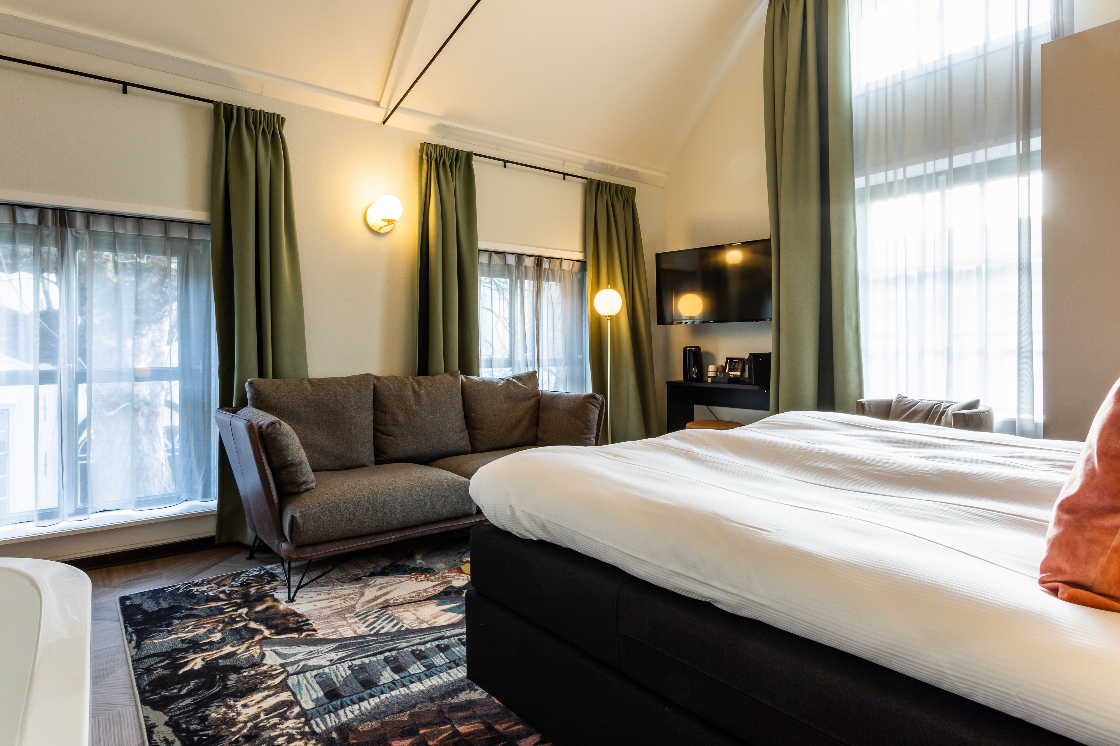 Habitación de hotel con una cama grande, un sofá, un televisor de pantalla plana y una alfombra estampada.
