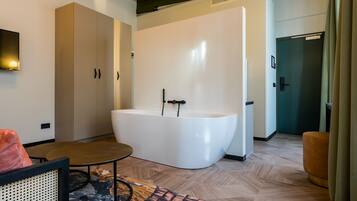 A modern bathroom with a freestanding bathtub, a wooden floor, and a large wardrobe.