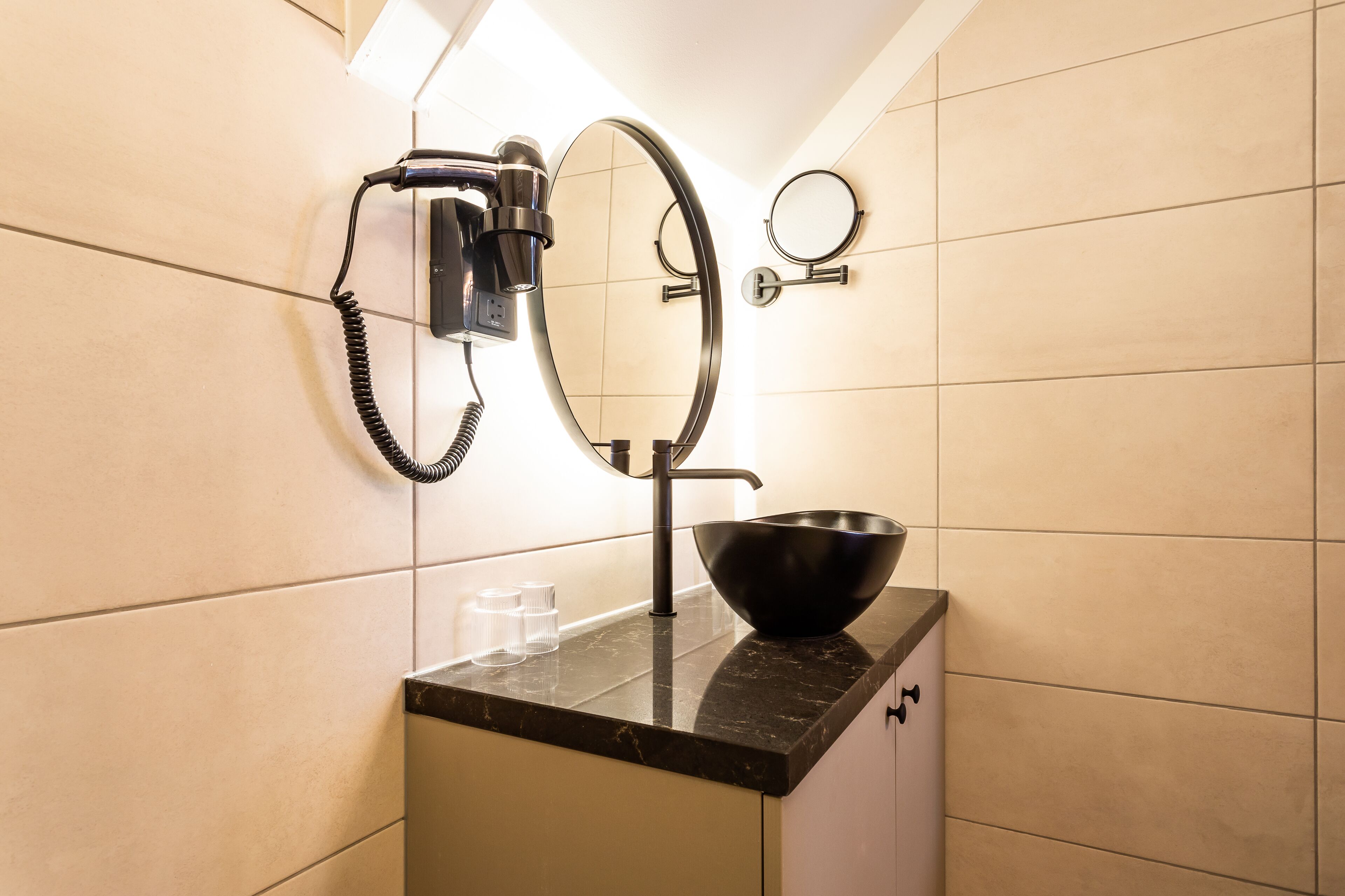 Un baño con encimera y lavabo negros, un secador de pelo y dos espejos.