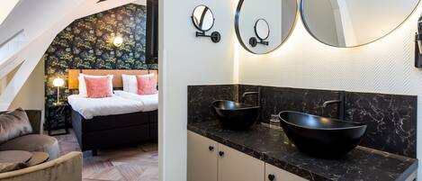 A modern bedroom with a bed, a nightstand, and a large mirror above a black marble countertop with a black sink.