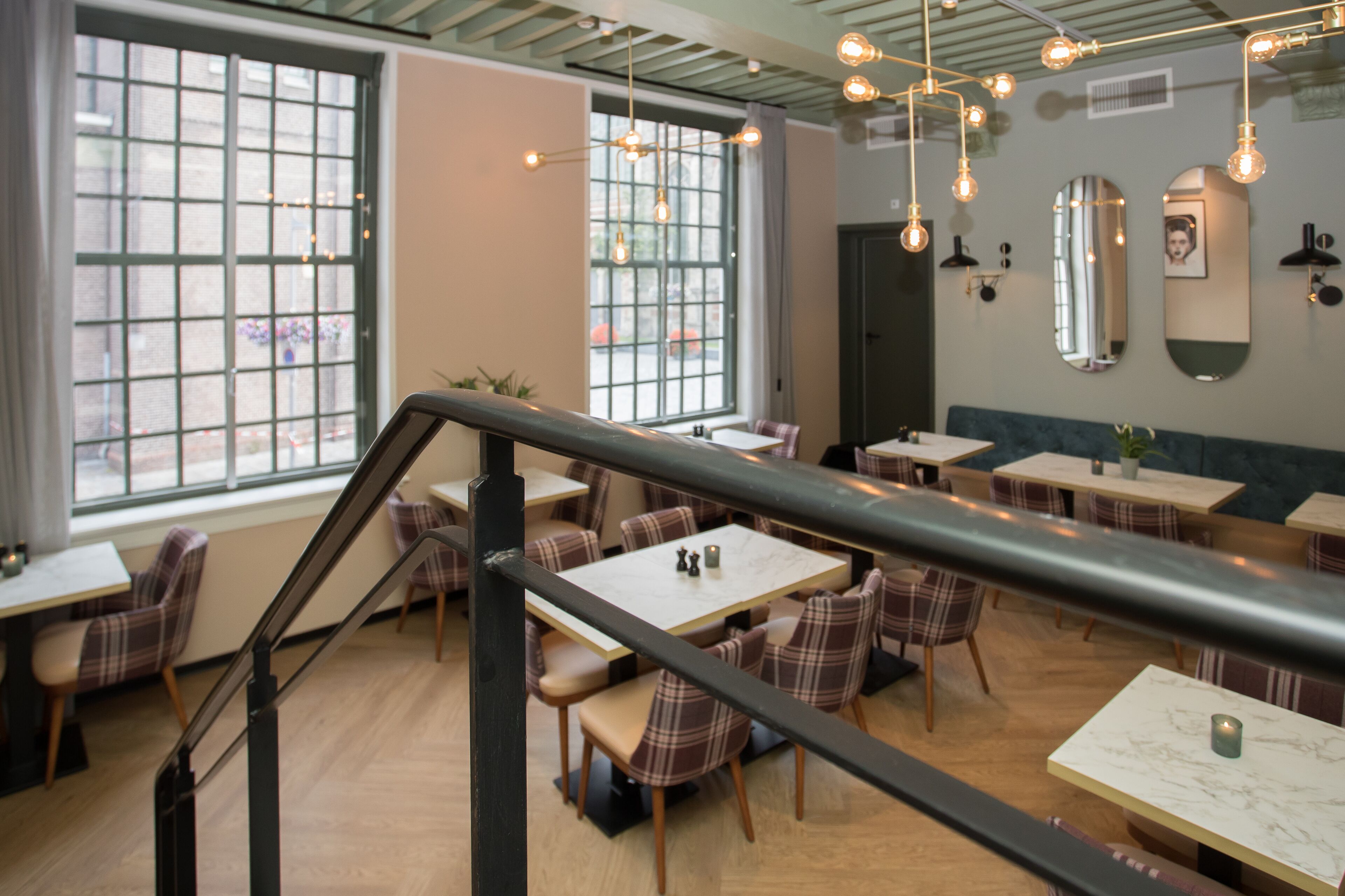 Un restaurant doté de nombreuses tables et chaises, d’un escalier et de luminaires suspendus.
