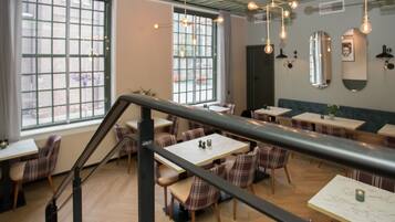 Un restaurant doté de nombreuses tables et chaises, d’un escalier et de luminaires suspendus.