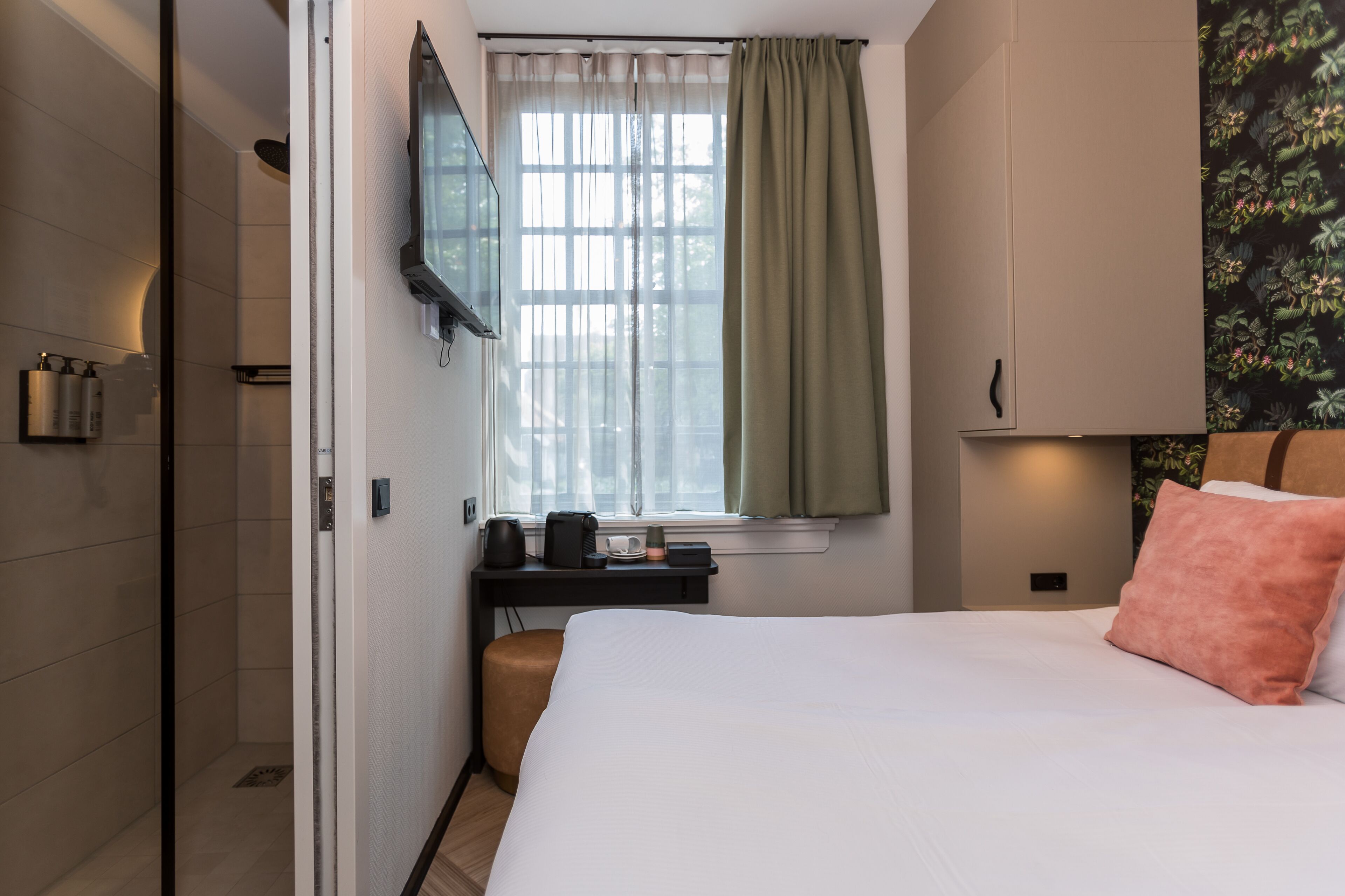 Una habitación de hotel con cama, escritorio con cafetera, televisión y ventana con cortinas.
