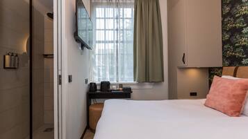 Una habitación de hotel con cama, escritorio con cafetera, televisión y ventana con cortinas.