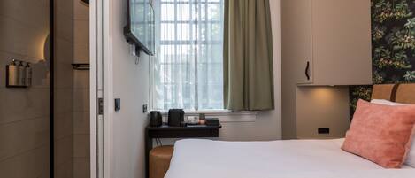 A hotel room with a bed, a desk with a coffee maker, a TV, and a window with curtains.