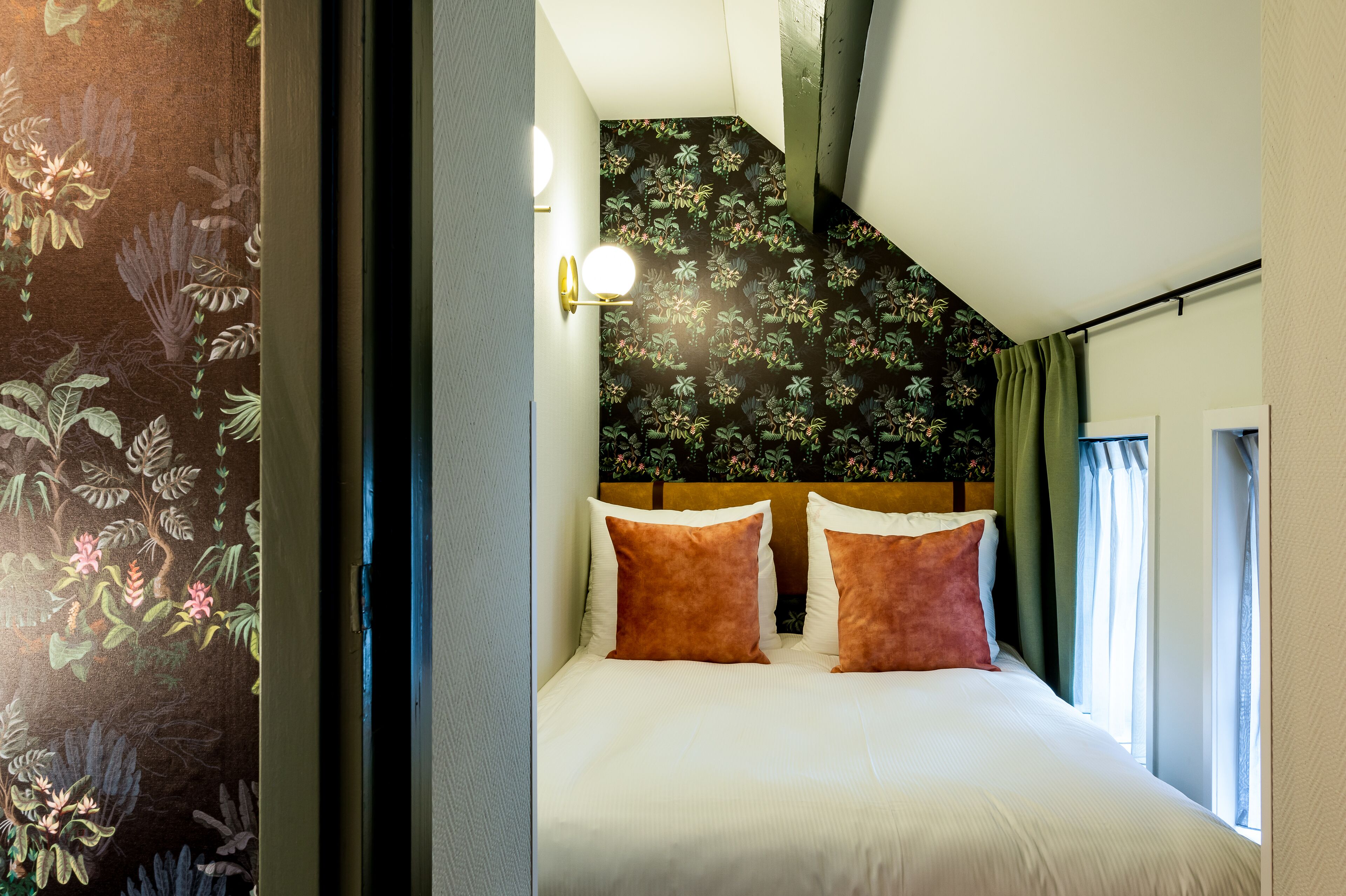 Une chambre à coucher avec un lit, deux oreillers, une tête de lit et une fenêtre avec des rideaux.