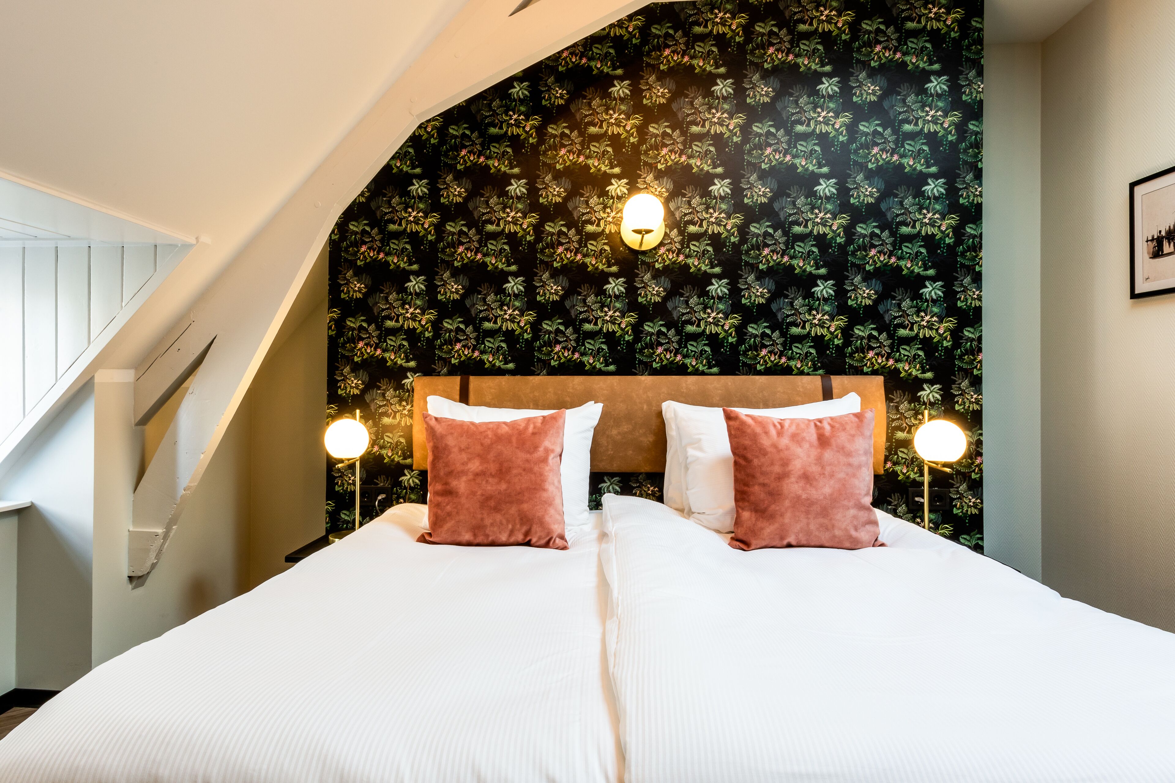 A bedroom with a bed, two nightstands, a headboard with a floral wallpaper, and a staircase.