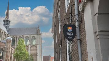 Une enseigne d’hôtel, avec un logo et un nom, fixée à un bâtiment dont la façade est en briques, avec une église en arrière-plan.