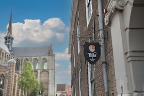 A hotel sign with a logo and name, attached to a building with a brick facade and a church in the background.